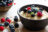 A bowl of oatmeal topped with blueberries, raspberries, blackberries, and mint leaves, with a basket of berries in the background.